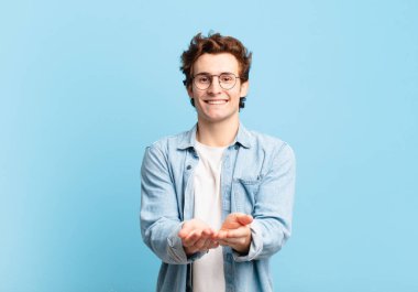 Genç yakışıklı çocuk mutlu bir şekilde gülümsüyor, arkadaş canlısı, kendinden emin, pozitif bakışlı, bir nesne ya da konsept sunuyor ve gösteriyor.