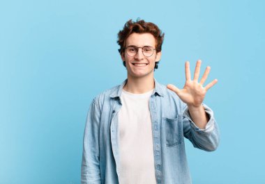 Genç yakışıklı çocuk gülümsüyor ve arkadaş canlısı görünüyor, 5 ya da 5 numarayı gösteriyor, elleri önde, geriye doğru sayıyor.