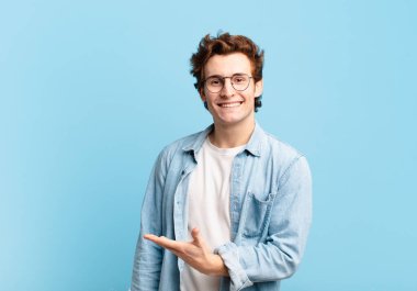 Genç yakışıklı çocuk neşeyle gülümsüyor, mutlu hissediyor ve fotokopi uzayında bir konsept gösteriyor.