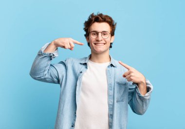 Genç yakışıklı çocuk, kendine güvenerek gülümsüyor. Geniş bir gülümseme, pozitif, rahat, tatmin olmuş bir tavır sergiliyor.