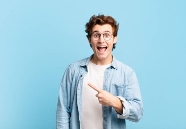 Genç yakışıklı çocuk heyecanlı ve şaşırmış görünüyor. Yana ve yukarı doğru uzayı gösteriyor.