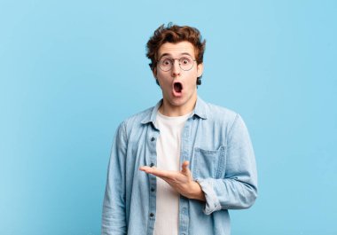 Genç yakışıklı çocuk şaşırmış ve şoka uğramış görünüyor, çenesi düşmüş, eli açık bir nesneyi tutuyor.