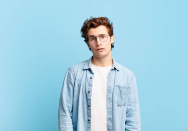 young handsome boy feeling puzzled and confused, with a dumb, stunned expression looking at something unexpected