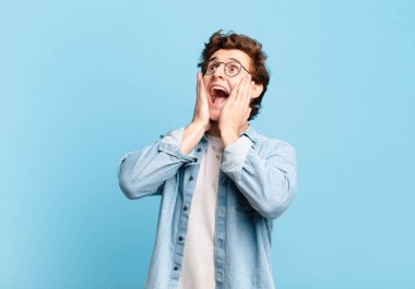 Genç yakışıklı çocuk mutlu, heyecanlı ve şaşırmış hissediyor, iki eli yüzü yana bakıyor.