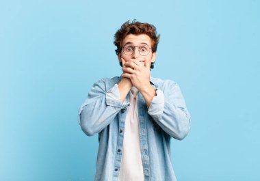 Şok olmuş, şaşırmış bir ifadeyle ağzı kapatan genç yakışıklı bir çocuk, sır saklıyor ya da 