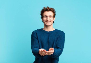 Genç yakışıklı çocuk mutlu bir şekilde gülümsüyor, arkadaş canlısı, kendinden emin, pozitif bakışlı, bir nesne ya da konsept sunuyor ve gösteriyor.