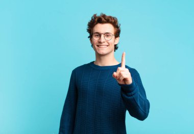 Genç yakışıklı çocuk gururla gülümsüyor ve gururla bir numaralı pozunu veriyor, kendini lider gibi hissediyor.