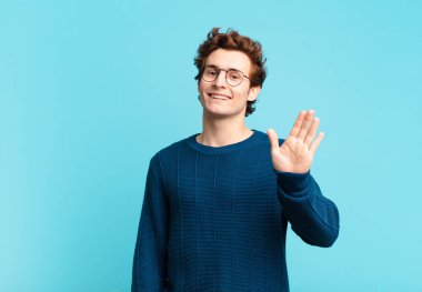 Genç yakışıklı çocuk mutlu ve neşeyle gülümsüyor, el sallıyor, seni selamlıyor ve selamlıyor, ya da hoşça kal diyor.