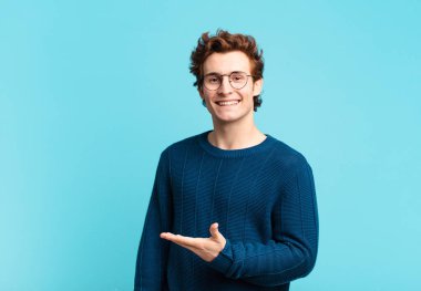 Genç yakışıklı çocuk neşeyle gülümsüyor, mutlu hissediyor ve fotokopi uzayında bir konsept gösteriyor.