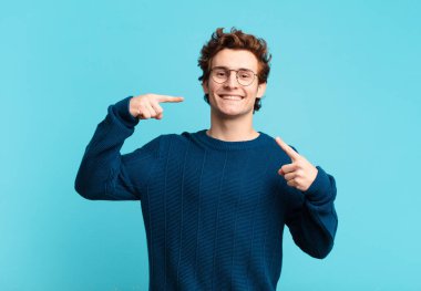 Genç yakışıklı çocuk, kendine güvenerek gülümsüyor. Geniş bir gülümseme, pozitif, rahat, tatmin olmuş bir tavır sergiliyor.