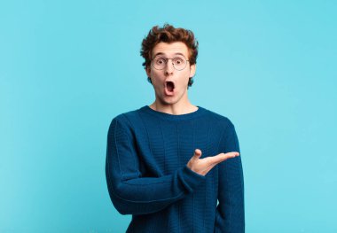 Genç yakışıklı çocuk şaşırmış ve şoka uğramış görünüyor, çenesi düşmüş, eli açık bir nesneyi tutuyor.