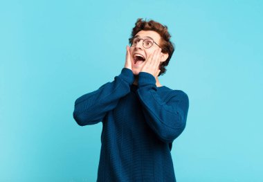 Genç yakışıklı çocuk mutlu, heyecanlı ve şaşırmış hissediyor, iki eli yüzü yana bakıyor.