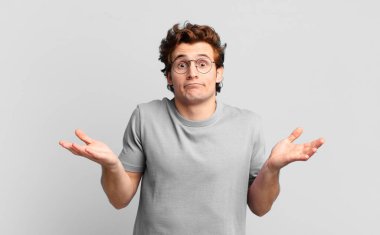 Genç yakışıklı çocuk şaşkın ve şaşkın, şüpheci, farklı seçenekleri tartıyor ya da komik bir ifadeyle seçiyor.