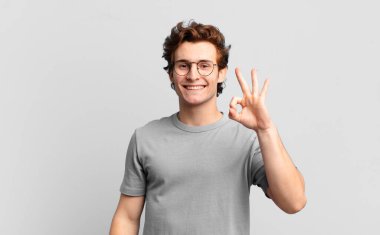 Genç yakışıklı çocuk kendini mutlu, rahat ve tatmin olmuş hissediyor, iyi bir jestle onaylıyor, gülümsüyor.