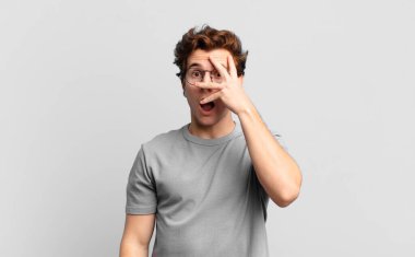 Genç yakışıklı çocuk şok olmuş, korkmuş ya da korkmuş görünüyor. Yüzü elle kaplanmış ve parmaklarının arasından gizlice bakıyor.