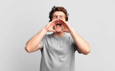 Genç yakışıklı çocuk mutlu, heyecanlı ve pozitif hissediyor. Elleri ağızda, bağırıyor.