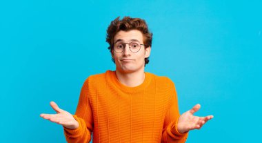 Genç yakışıklı çocuk şaşkın ve şaşkın, şüpheci, farklı seçenekleri tartıyor ya da komik bir ifadeyle seçiyor.