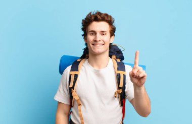 Yürüyüşçü çocuk gülümsüyor ve arkadaş canlısı görünüyor, bir numarayı gösteriyor ya da ilk eli önde, geri sayıyor.