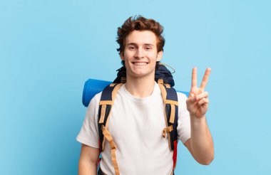 Yürüyüşçü çocuk gülümsüyor ve arkadaş canlısı görünüyor, iki ya da iki numarayı gösteriyor, elleri önde, geri sayıyor.