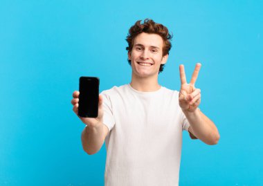 Genç bir çocuk gülümsüyor ve mutlu görünüyor, tasasız ve olumlu, tek elle zafer ya da barış işareti yapıyor. telefon ekranı kavramı