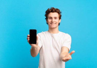 Genç çocuk mutlu bir şekilde gülümsüyor, kendine güvenen, olumlu bakışla, bir nesne ya da konsept sunuyor ve gösteriyor. telefon ekranı kavramı