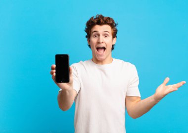 Genç çocuk kendini mutlu, heyecanlı, şaşırmış ya da şok olmuş hissediyor. İnanılmaz bir şeye gülümsüyor ve hayrete düşüyor. telefon ekranı kavramı