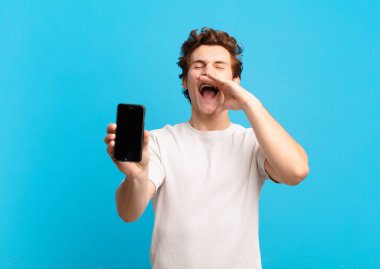Genç çocuk mutlu, heyecanlı ve pozitif hissediyor. Elleri ağızda, bağırarak bağırıyor. telefon ekranı kavramı