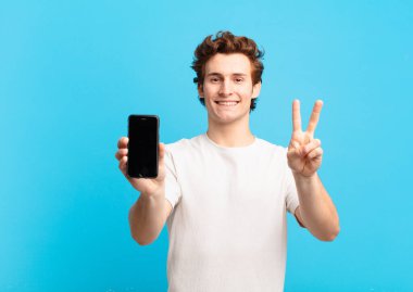 Genç bir çocuk gülümsüyor ve arkadaş canlısı görünüyor. İki ya da iki numarayı gösteriyor. Elleri önde, geriye doğru sayıyor. telefon ekranı kavramı
