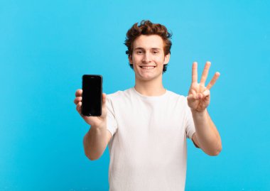 Genç çocuk gülümsüyor ve arkadaş canlısı görünüyor, üç ya da üç numarayı gösteriyor, eli önde, geri sayıyor. telefon ekranı kavramı
