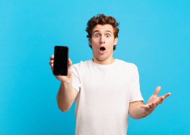 Delikanlı ağzı açık ve şaşırmış, şok olmuş ve inanılmaz bir sürprizle şaşkına dönmüş. telefon ekranı kavramı