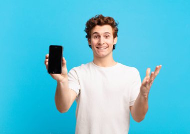 Genç bir çocuk mutlu, şaşırmış ve neşeli, olumlu bir tavırla gülümseyen, bir çözüm ya da fikir gerçekleştiren. telefon ekranı kavramı