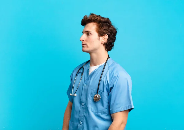 young nurse man on profile view looking to copy space ahead, thinking, imagining or daydreaming