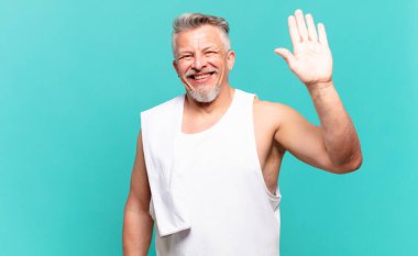 Kıdemli sporcu mutlu ve neşeli bir şekilde gülümser, el sallar, sizi karşılar ve selamlar, ya da elveda der.