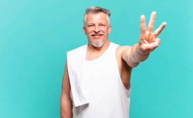 Kıdemli sporcu gülümsüyor ve arkadaş canlısı görünüyor. Üç ya da üç numarayı gösteriyor. Elleri önde, geri sayıyor.