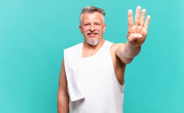 Kıdemli sporcu gülümsüyor ve arkadaş canlısı görünüyor. Elleri önde, geriye doğru sayıyor.