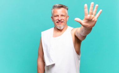 Kıdemli sporcu gülümsüyor ve arkadaş canlısı görünüyor. 5 ya da 5 numarayı gösteriyor. Elleri önde, geriye doğru sayıyor.