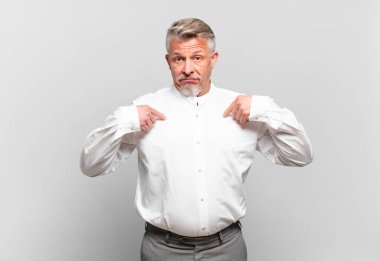 Kıdemli işadamı mutlu, şaşkın ve gururlu hissediyor, heyecanlı ve şaşkın bir bakışla kendini işaret ediyor.