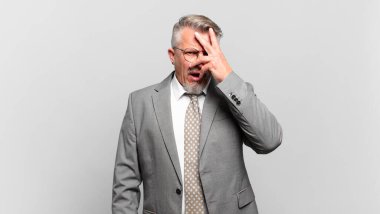 Kıdemli işadamı şok olmuş, korkmuş ya da korkmuş görünüyor. Yüzü elle örtülmüş ve parmaklarının arasından gizlice bakıyor.