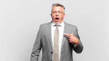 Kıdemli işadamı ağzı açık, şaşkın ve şaşkın bir şekilde kendini işaret ediyor.