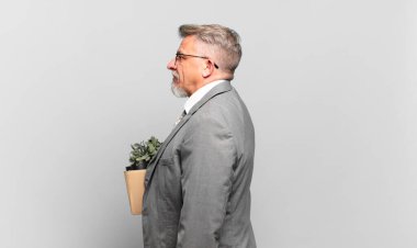 Emekli kıdemli işadamı profil görünümünde ilerideki boşluğu kopyalamaya çalışıyor, düşünüyor, hayal ediyor ya da hayal kuruyor.