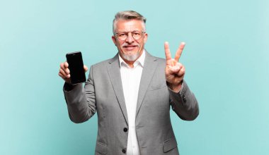 Kıdemli iş adamı gülümsüyor ve arkadaş canlısı görünüyor. İki ya da iki numarayı gösteriyor. Elleri önde, geri sayıyor.