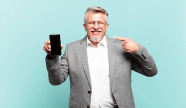 Kıdemli işadamı gülümseyerek kendi geniş gülümsemesine, pozitif, rahat, tatmin olmuş tavrına işaret ediyor.