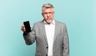 Kıdemli işadamı şaşırmış ve kafası karışmış görünüyor. Sinirli bir hareketle dudağını ısırıyor. Sorunun cevabını bilmiyor.