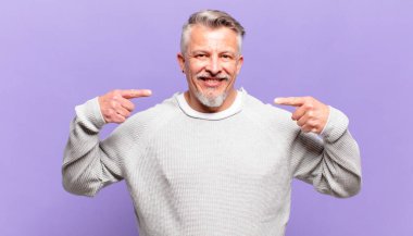 old senior man smiling confidently pointing to own broad smile, positive, relaxed, satisfied attitude