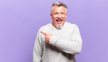 old senior man looking excited and surprised pointing to the side and upwards to copy space