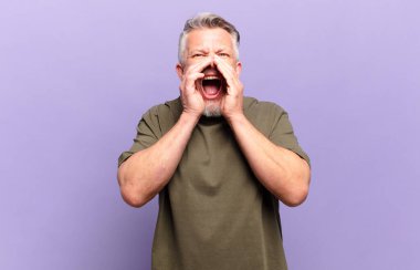 old senior man feeling happy, excited and positive, giving a big shout out with hands next to mouth, calling out