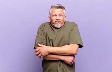 old senior man shrugging, feeling confused and uncertain, doubting with arms crossed and puzzled look