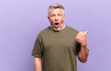 old senior man looking astonished in disbelief, pointing at object on the side and saying wow, unbelievable