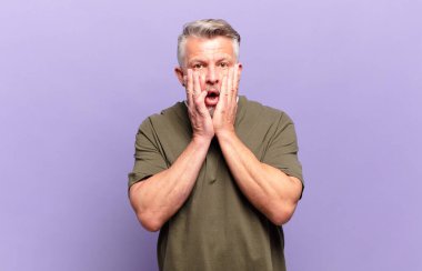 old senior man feeling shocked and scared, looking terrified with open mouth and hands on cheeks