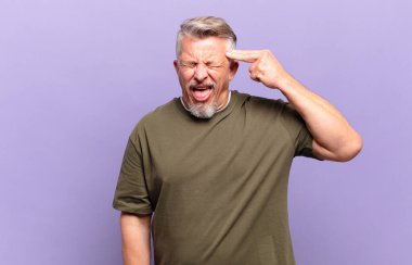 old senior man looking unhappy and stressed, suicide gesture making gun sign with hand, pointing to head
